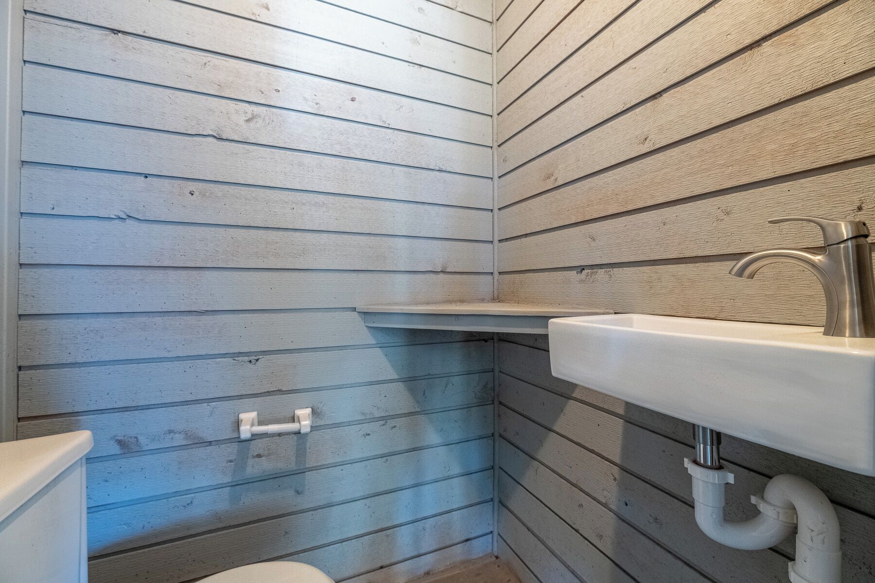 A bathroom with wooden paneling, a white sink, and a toilet.