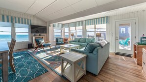 A coastal living room with a large window, a sofa, a coffee table, and a TV. - York - Duck, Carolina Dunes, Oceanfront, Ocean View, Hot Tub, Large Decks, Pets OK (Duck)