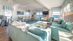 A living room with a sofa, chairs, a TV, and a view of the sea. - York - Duck, Carolina Dunes, Oceanfront, Ocean View, Hot Tub, Large Decks, Pets OK (Duck)