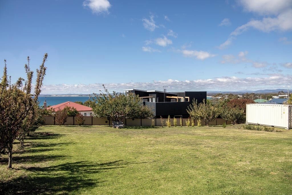 A residential area with a modern house, a fenced yard, and a view of the sea.