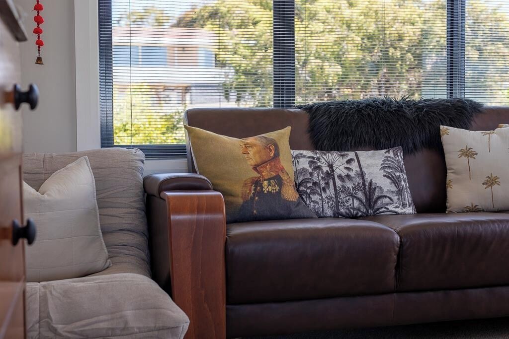 A brown leather sofa with decorative pillows and a fur throw, positioned near a window with blinds.