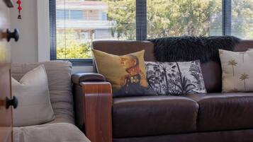 A brown leather sofa with decorative pillows and a fur throw, positioned near a window with blinds.