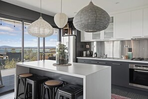 A modern kitchen with a central island, bar stools, stainless steel appliances, and pendant lighting.