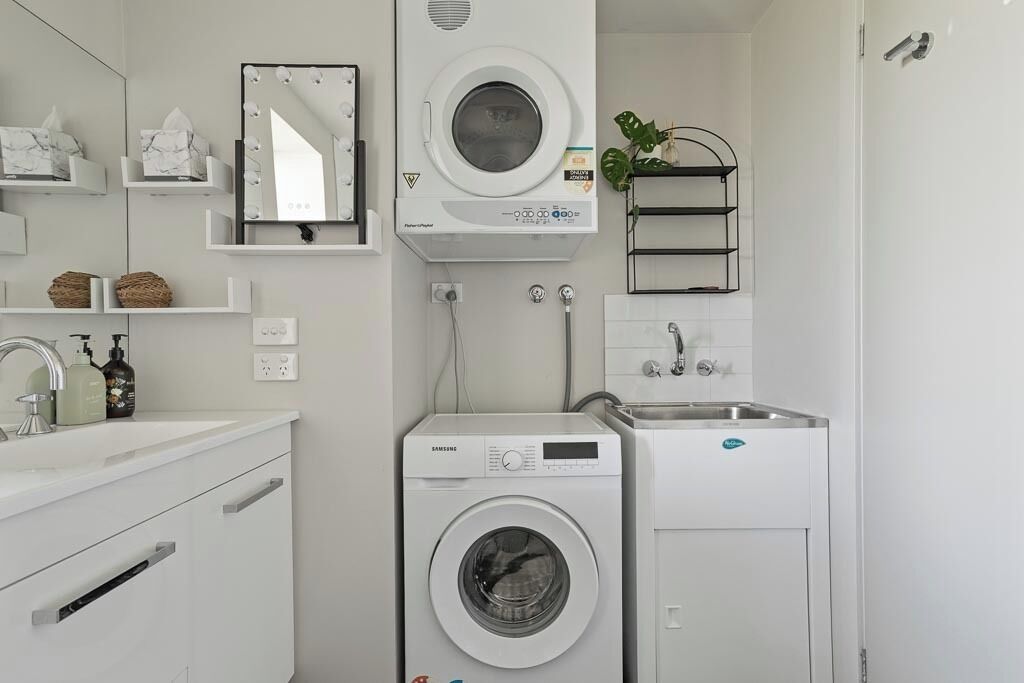 Une salle de bain moderne équipée d’un lave-linge et d’un sèche-linge intégrés, d’un meuble-lavabo avec miroir et d’une étagère pour les articles de toilette.