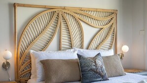 Ein Bett mit einem gewobenen Kopfteil, weißer Bettwäsche und zwei Nachttischlampen.