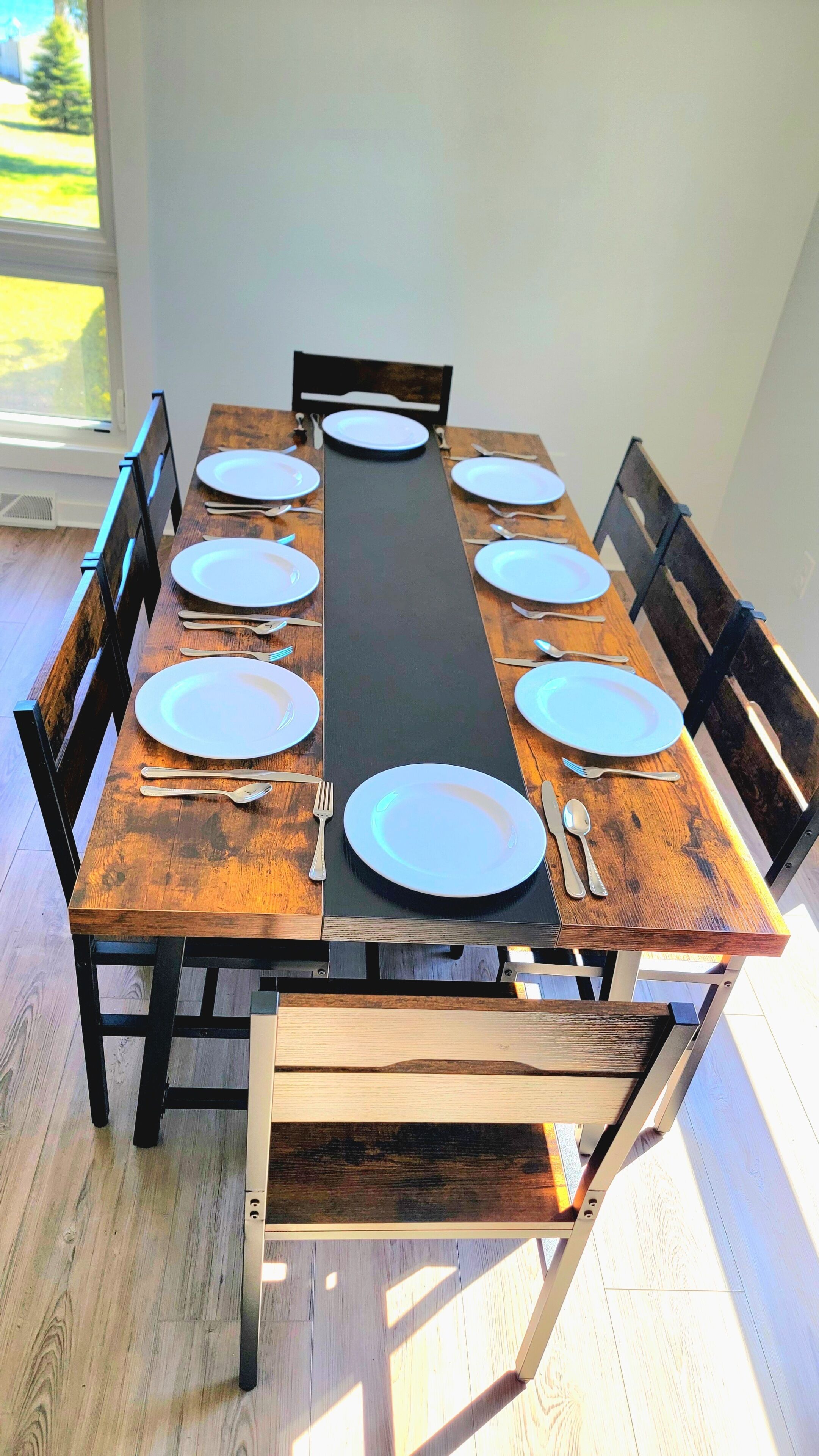 A rectangular dining table with a black center runner, surrounded by wooden chairs with black metal frames.