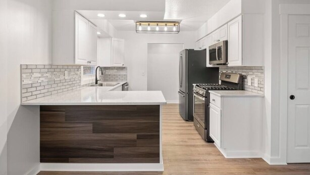 Una cocina moderna con armarios blancos, una isla central, estufa integrada y un microondas.