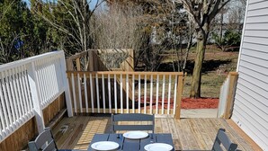 Una terraza de madera con una mesa rectangular y seis sillas, rodeada por una cerca blanca.