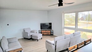 Una sala de estar moderna con una televisión de pantalla plana, dos sofás, una mesa de centro y un ventanal grande.
