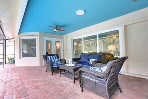 Ein überdachter Patio-Bereich mit Korbmöbeln, einem Deckenventilator und großen Fenstern.