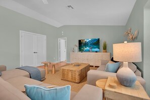 Ein modernes Wohnzimmer mit einer Couch, einem Couchtisch und einem Fernseher, der eine malerische Landschaft zeigt.