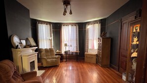 A room with a fireplace, two armchairs, a wooden floor, and a cabinet with glass doors. - Traditional Bed & Breakfast in Irvine KY with Swimming pool, Wi-Fi Room 2 (Irvine)