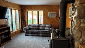 A cozy room with a plaid sofa, a television, a radio, a fireplace, and a stone wall.