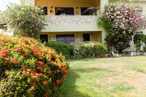 A two-story building with a stone facade, a balcony, and a well-maintained garden with various shrubs and flowers. - Nice 2-bedroom house with AC in delightful Saint Johns (Saint Johns)