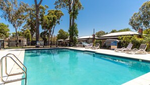 Una piscina con sillas de descanso y un área cercada, rodeada de árboles y edificios.