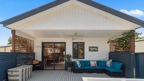 A covered patio with a ceiling fan, a sofa with cushions, and a wooden fence.