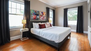 Un dormitorio con una cama, una mesita de noche, una lámpara y una obra de arte en la pared.