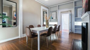 Un comedor con una mesa blanca y sillas marrones, un florero con flores y un espejo en la pared.