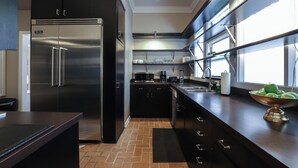 Cocina moderna con refrigerador de acero inoxidable, gabinetes negros, encimera de madera y ventana que deja entrar luz natural.