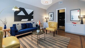 Una sala moderna con un sofá azul, un sillón amarillo, una mesa redonda y un cuadro abstracto grande en la pared.
