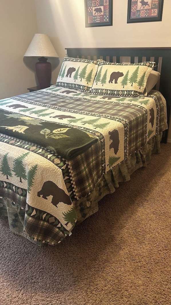 A bed with a quilted blanket featuring animal and tree patterns, a bedside lamp, and a framed picture on the wall.