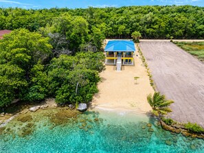 En fastighet vid stranden med ett hus, kristallklart turkosfärgat vatten och tät vegetation.
