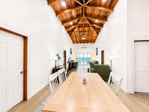 A spacious dining area with a long wooden table, white walls, and a high wooden ceiling. - Family friendly beach front two-bedroom home with AC (Hopkins)