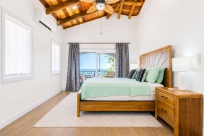 A bedroom with a wooden ceiling, a bed with a green bedspread, a nightstand, and a view of the outdoors. - Family friendly beach front two-bedroom home with AC (Hopkins)