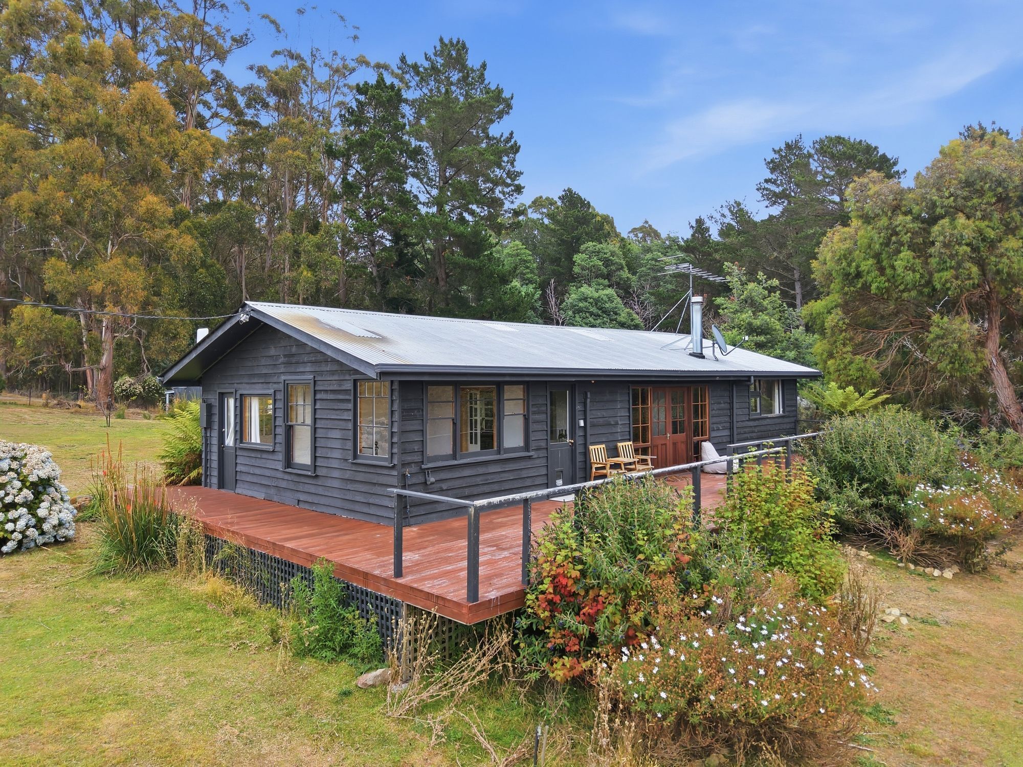 A two-story cabin with a deck, surrounded by trees and vegetation.