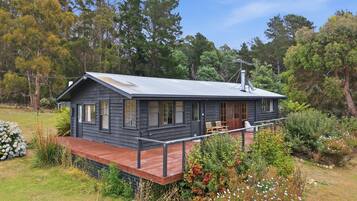 A two-story cabin with a deck, surrounded by trees and vegetation.