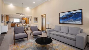 A modern living room with a grey sofa, two armchairs, a coffee table, and a painting of a blue ocean scene. - Luxurious oceanfront 2-bedroom suite located on pristine beach in Cabo San Lucas (San José del Cabo)