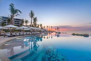 Ein Hotelpool mit Liegestühlen, Sonnenschirmen und Palmen.
