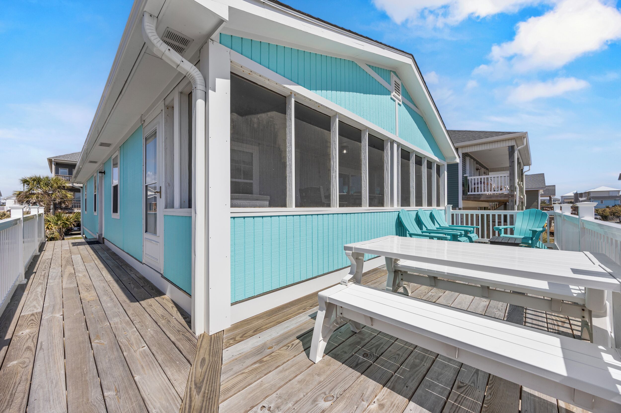 Une maison située sur la côte, dotée d’une terrasse en bois, de grandes fenêtres et d’un espace salon extérieur.