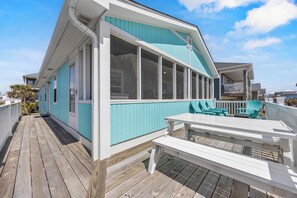Uma casa à beira-mar com deck de madeira, janelas amplas e área de estar externa.
