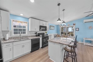 A modern kitchen with white cabinets, a granite countertop, a built-in oven, and a bar area with stools. - Dolly's Dream 2nd Row Retreat w Ocean Views Screened Porch & Pet-Friendly living on Topsail (Surf City)