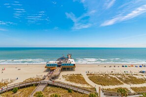 A beachside building with a pier, a lifeguard tower, and a sandy beach with umbrellas. - Yachtsman S805 1 BR (Myrtle Beach)