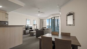 Una habitación de hotel moderna con zona de comedor, sofá, televisor y balcón con vistas.