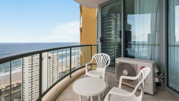 A balcony with a view of the ocean, a white table, two white chairs, and an air conditioning unit.