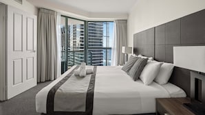 Habitación de hotel con una cama grande, televisión, mesita de noche, ventana con cortinas y vista a edificios.