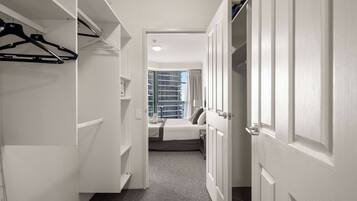 A hallway leading to a bedroom with a bed, a window, and a closet with hanging clothes.