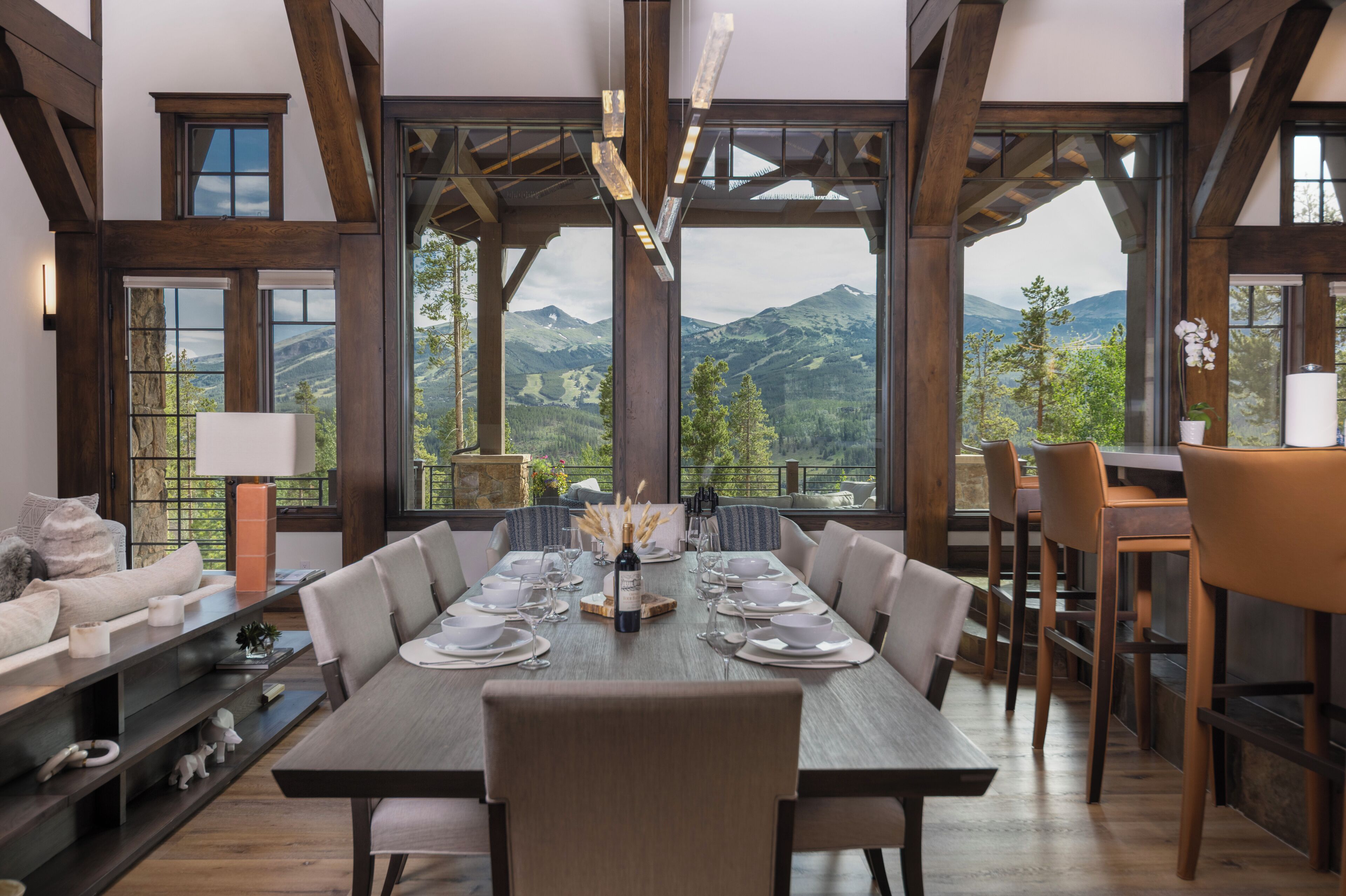 A dining area with a table set for six, large windows, and a view of mountains.
