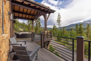 Una terraza de madera con mobiliario exterior, un muro de piedra y vistas a montañas.