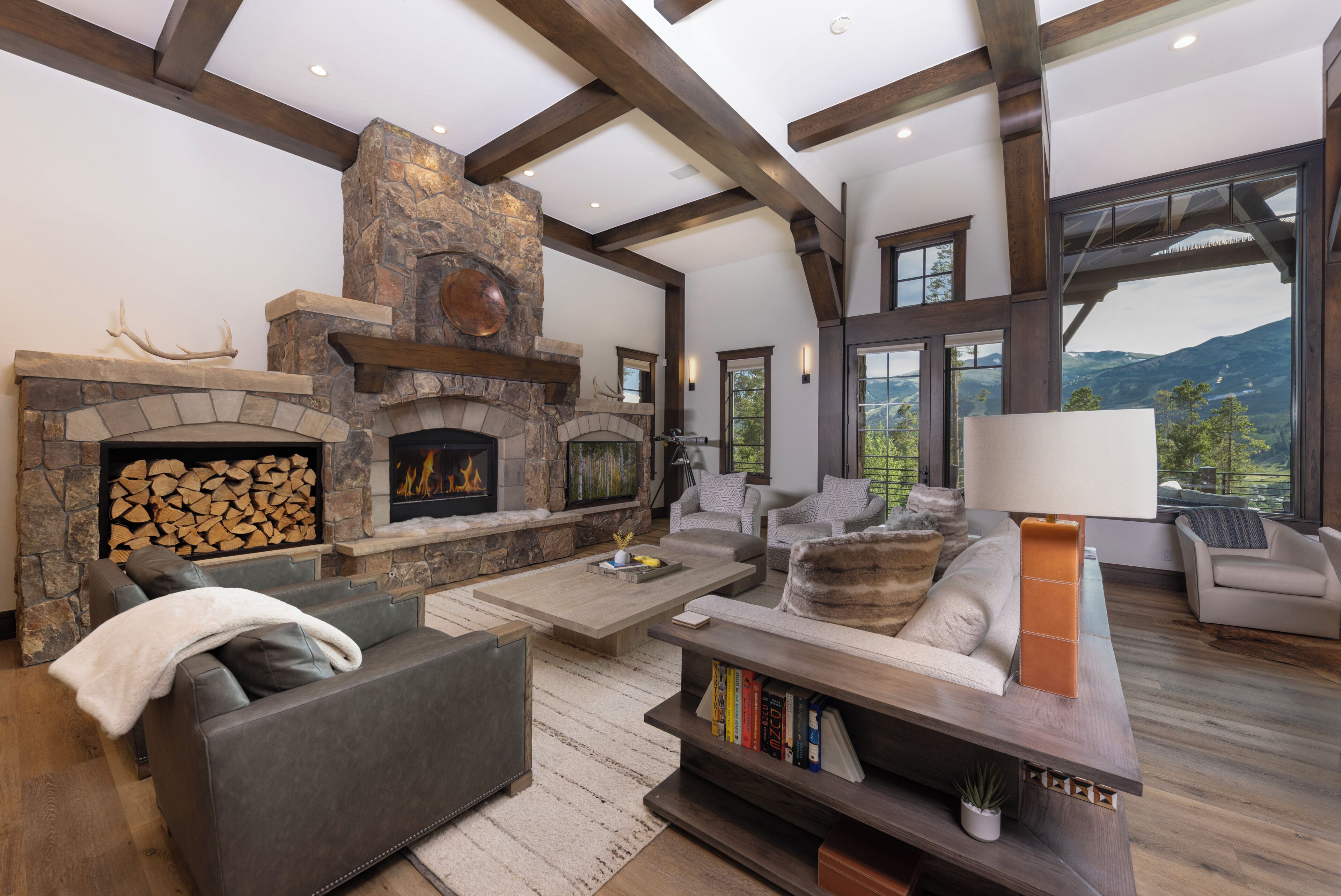 A spacious living room with a stone fireplace, comfortable seating, and large windows offering a mountain view.