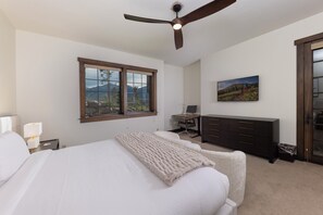 A bedroom with a bed, a desk, a chair, a dresser, a ceiling fan, a window with a view, and a painting on the wall. - Unmatched Elegance, Pool Table, Hot Tub, Ski Shuttle, Fire PIt with Views!! (Breckenridge)