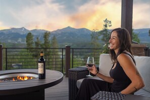 A person seated on a sofa with a bottle of wine and a glass on a table, overlooking a mountainous landscape. - Unmatched Elegance, Views, Amenities, and Location! (Breckenridge)