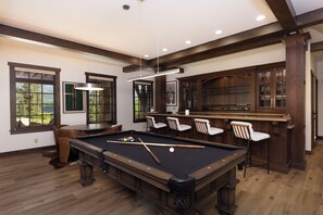 A pool table with chairs and a bar area in a room with wooden floors and large windows. - Unmatched Elegance, Views, Amenities, and Location! (Breckenridge)
