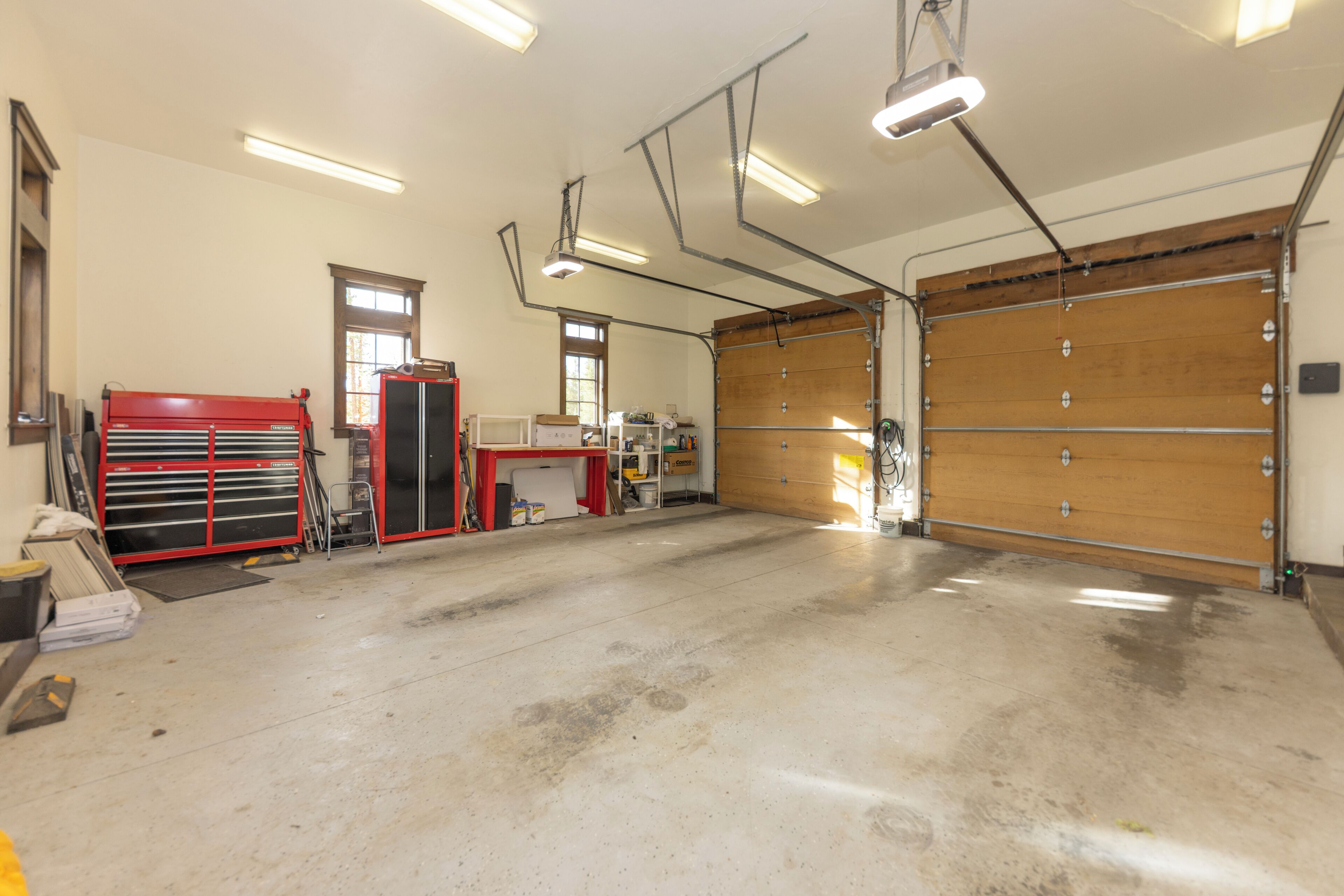 A spacious garage with a large workbench, tool cabinets, and a wooden garage door.