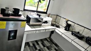 Cuina compacta amb nevera, cafetera i finestra amb vista a vegetació.