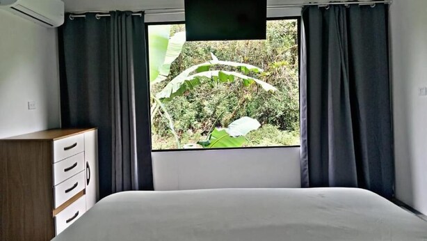 Un dormitori amb un llit, una televisió, una finestra amb cortines i un taulell.