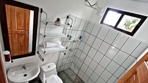 Un bany petit i funcional amb un lavabo, vàter i una petita prestatgeria amb articles de tocador.